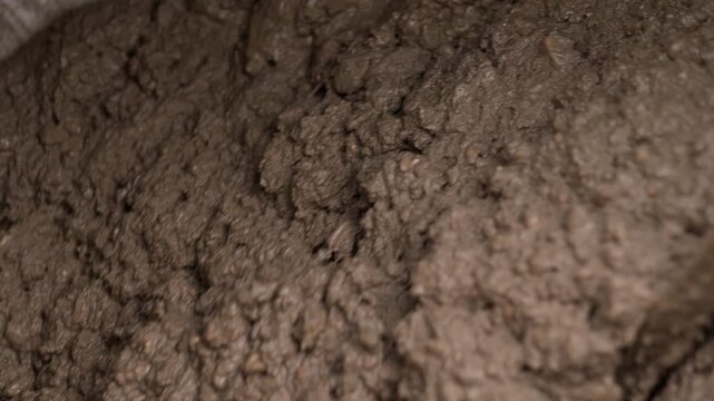 Macro view of wet brown mud with clumps, glossy damp sheen, ridged granular texture, and soft blur that suggests shifting earth slurry. Thick wet paste covers uneven ground, seen in surface detail.