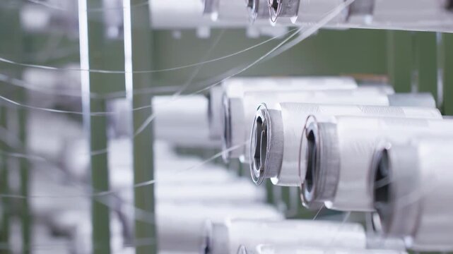Industrial automation factory production line weaving of polypropylene yarn spools bags textile spinning machine. White thread reels ropes making plastic sacks or fabric process in nylon manufacture