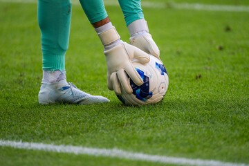 Close-up of soccer goalkeeper's gloved hands takeing a football on green grass during a professional match, highlighting goalkeeping technique and sports action. © Dziurek