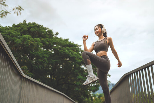 Active young woman exercising outdoors with headphones, performing high knee movement during fitness workout, enjoying energetic training, healthy lifestyle, cardio exercise and active recreation in p