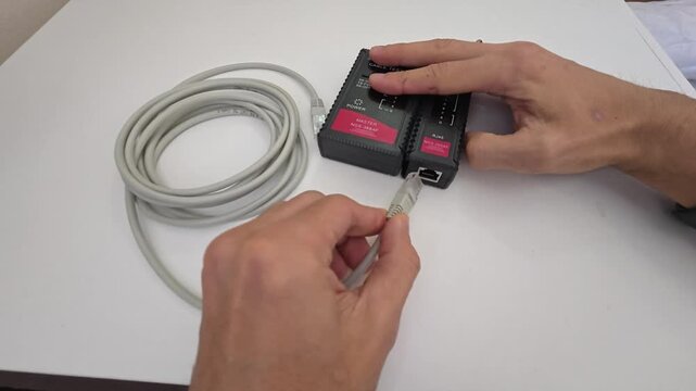Technician tests Ethernet cable with handheld cable tester, plugging connectors into master and remote units. Green indicator lights verify wire sequence during practical network connection check.
