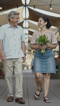 Vertical video: Offering father giving greens to daughter in denim skirt shopping market, smiling