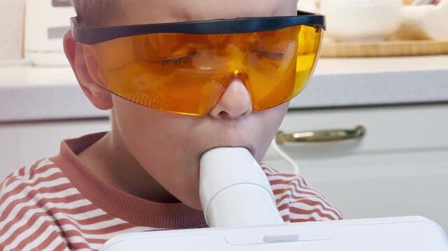 A young boy wearing protective orange goggles receives inhalation therapy at home. His quiet expression reflects patience, trust, and a feeling of brave hope.