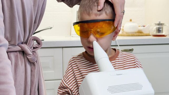 A young boy wearing protective orange goggles receives inhalation therapy as his mother gently holds his head at home. The tender care gives a reassuring feeling of love and comfort.