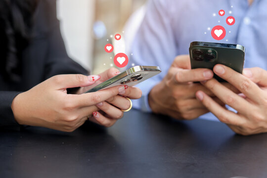 close up couple man and woman hold smartphone and using dating application to talk and make conservation and give love sign (heart) to each other while sitting together in cafe for romantic lifestyle