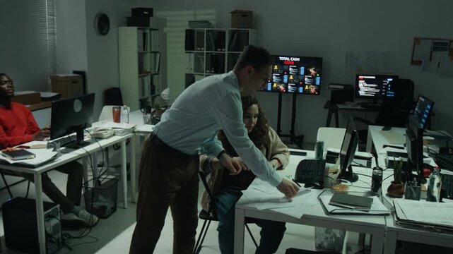 Caucasian young manager discussing paperwork and delegating tasks to diverse coworkers in dark scam office. Footage suitable for cybercrime and scam awareness campaign