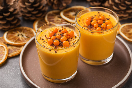 Two portion mousse of sea-buckthorn berries with black chocolate served in glasses on a dark stone table. Pine cones in background. Autumn and winter berry dessert.