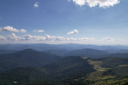 Aerial view of green mountain ridges and vast valleys under blue sunny sky with fluffy white clouds, drone panoramic shot of spectacular highlands wilderness landscape in summer, carpathians