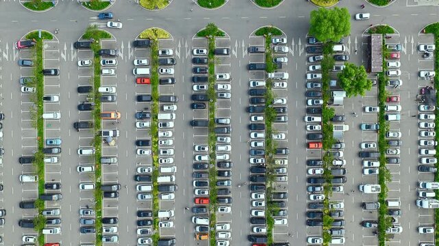 Aerial top down view of a large outdoor parking lot filled with many vehicles organized in neat rows during daytime.
