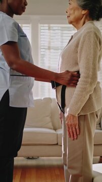 Vertical video: Leaning aide in scrubs fixing gait belt as senior rising safely at home, copy space