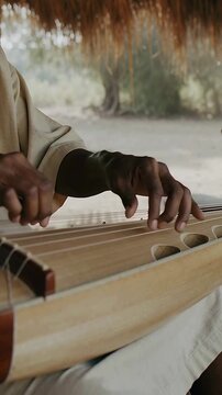 Vertical video: Hovering hands starting plucks on zither under thatched roof for practice