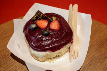 Cinnamon roll topped with dark berry glaze, fresh strawberries and blueberries, served on a wooden table, visible film grain. high quality photo © Татьяна Швец