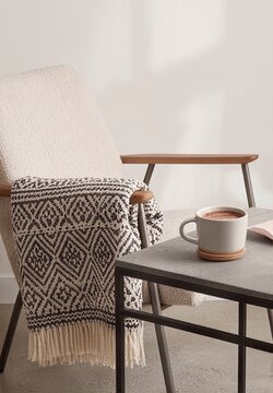 Cozy living room chair with patterned blanket and cup on table  