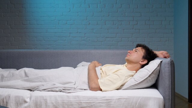 Young man lying awake in bed at night, staring at the ceiling, restless and anxious from insomnia and sleeplessness, struggling with stress, fatigue and quiet worry