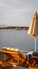 Fototapeta premium Wooden sun loungers with yellow striped towels on a seaside deck overlooking anchored boats