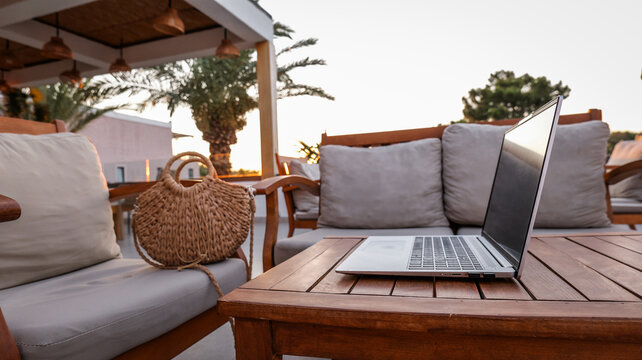 Open laptop on a wooden table at a cozy outdoor terrace during a warm golden hour sunset time