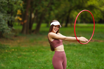 Athletic young woman exercising with hula hoop in park, space for text © New Africa