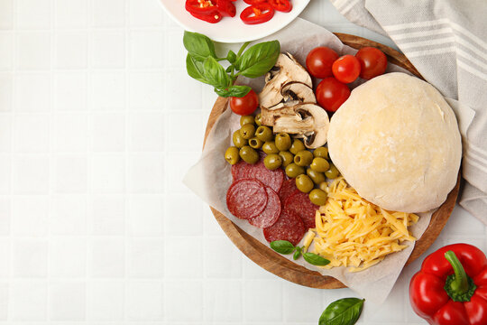 Making pizza. Dough and other different ingredients on white tiled table, top view. Space for text
