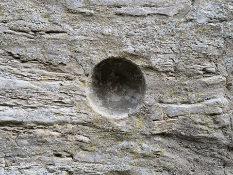textured stone surface with a distinct round cavity carved into it, representing historical stonemasonry, natural rock patterns, and ancient architectural details.