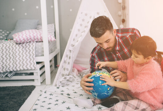 Cute little daughter and her handsome young dad iare playing together in child's room. Happy family of dady and child prepare to travel trip, learn for route map