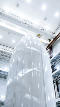 White aerospace rocket fuselage inside a large industrial facility with overhead cranes and bright lighting