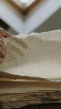 Vertical video: Sliding fingers lifting handmade sheet on table under skylight inspecting flecks