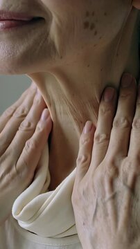 Vertical video: Hands reaching senior Asian woman lifting cream scarf at home, smoothing neck
