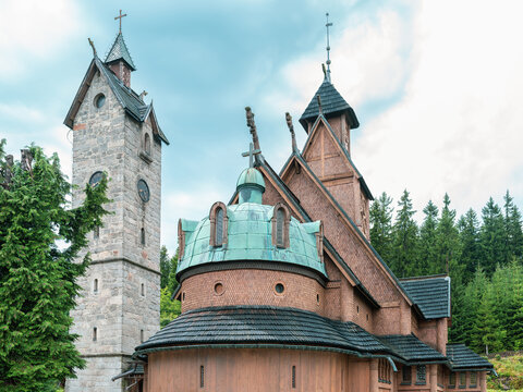 Historic Wang Stave Church in Karpacz, Poland, featuring traditional wooden architecture, a stone bell tower, and a green roof surrounded by pine trees.
