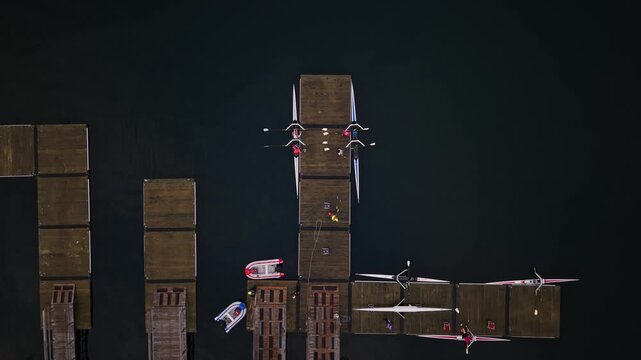 Aerial view of a rowing crew finishing practice at sunrise, arriving at a wooden pier in Halifax Harbour and carefully pulling their long racing boat onto the dock.