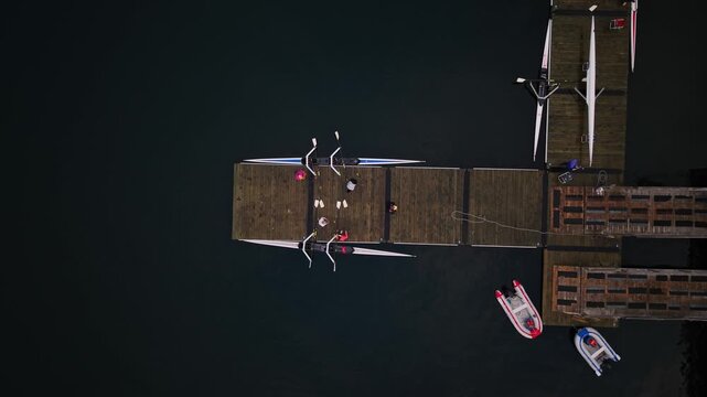 Drone footage of athletes completing a rowing session in Halifax, with the crew gathered at a wooden pier as they lift their racing shell out of the water after training.