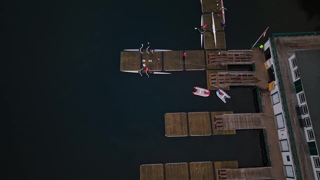 Cinematic aerial shot of rowers returning from morning practice, docking at a wooden pier and hauling their racing boats ashore after finishing their training in Halifax Harbour.
