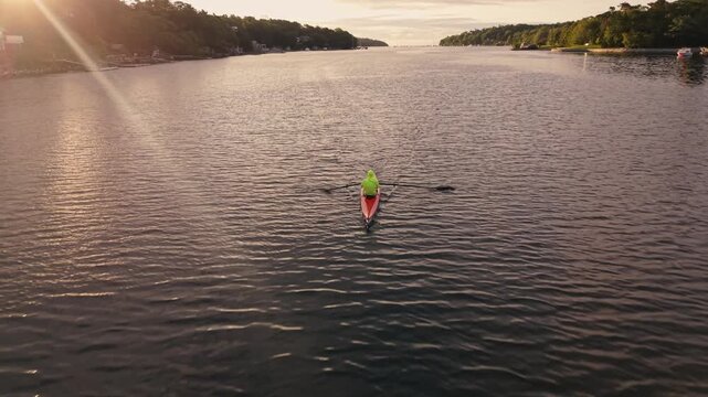 Aerial drone footage of Halifax Harbour at sunrise, capturing a rowing crew during early morning training as their racing shell moves smoothly across the calm coastal water.