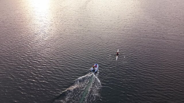 Wide aerial view of Halifax Harbour at sunrise, capturing competitive rowing athletes practicing in racing shells across the open water, with the Nova Scotia coastline visible in the distance.