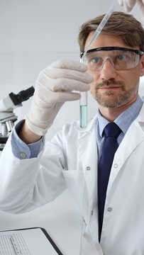 Scientist in lab coat and protective glasses analyzing green liquid in test tube with pipette in a professional laboratory. Medicine, health care and science concept