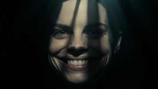 Woman with an unnatural wide smile emerging from the darkness. Creepy portrait in cinematic lighting. Horror concept representing psychological thriller film scene