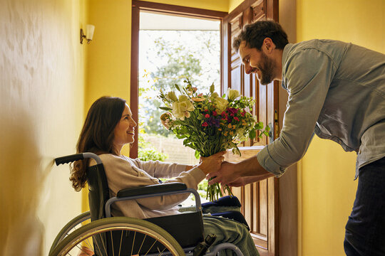 Man giving flowers to smiling woman in wheelchair at door