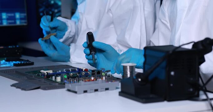 Technicians in protective gloves repair a circuit board with precision tools in a modern electronics laboratory.
