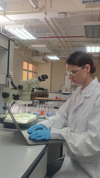 Lab or laboratory. Female scientist conducting laboratory research using lab tools. Such as microscope pipette and laptop to analyze samples and colorful bio chemical solutions in a modern laboratory