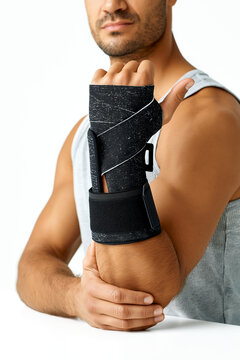 A close up of a muscular athletic man wearing a supportive black medical wrist brace or splint stabilizer on his injured hand, isolated on a clean white background.
