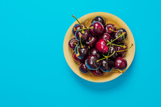 Bowl of fresh, glossy cherries sits on a bright blue background. Each cherry has a stem and deep red color. Image shows no people or animals. Perfect for food blogs, recipes, or healthy eating content