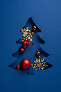 Merry Christmas and Happy New Year greeting with blue paper tree cutout and red ornaments on vertical blue background