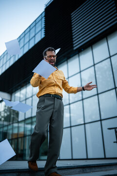 Stressed businessman yelling on phone throwing papers