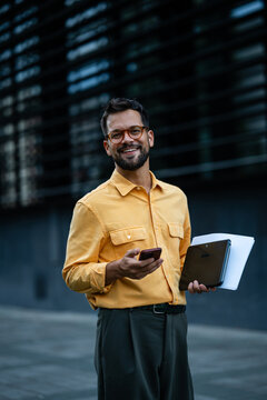 Smiling professional man using smartphone and carrying documents