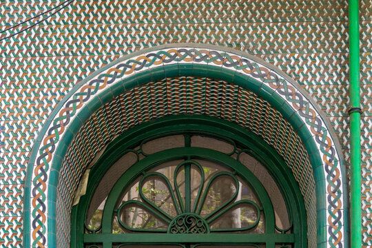 Tiled arch with intricate geometric and braided patterns above a distinctive green iron window grill