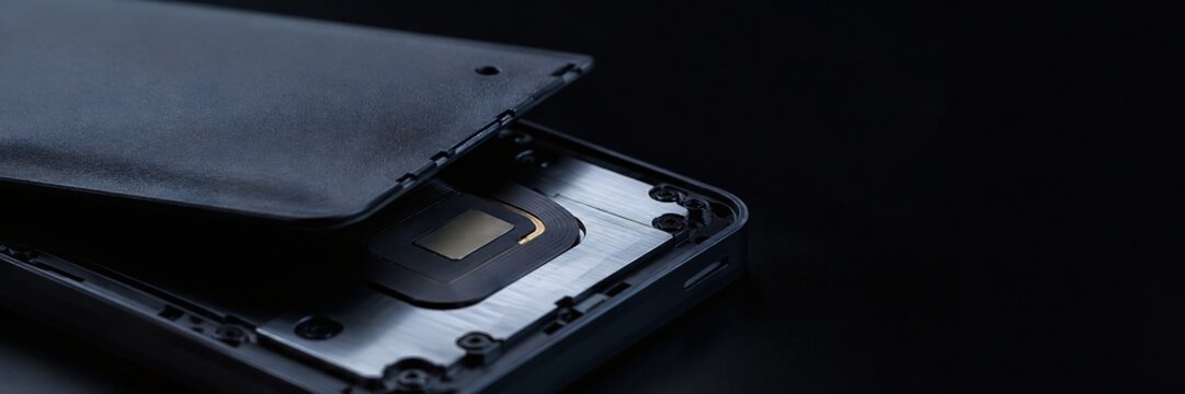 Macro panoramic view of disassembled mobile device interior displaying wireless induction charging coil and internal aluminum chassis on dark background