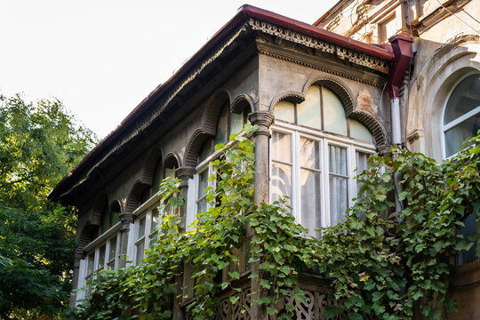 Historic residential building facade with traditional carved wooden balcony and greenery in Tbilisi Georgia, vintage exterior of weathered ancient house in old town, classic architectural heritage.
