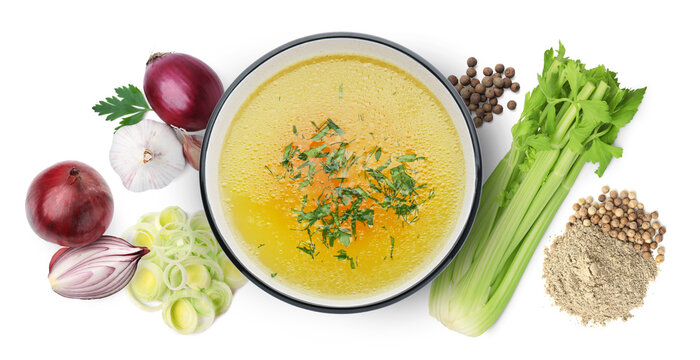 Broth in bowl, celery stalks, onions, garlic and peppercorns on white background, top view