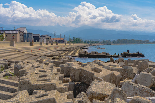 Concrete tetrapods in the foreground with a fishing village and mountains beneath dramatic cumulus clouds at Kurobe Port, Toyama.