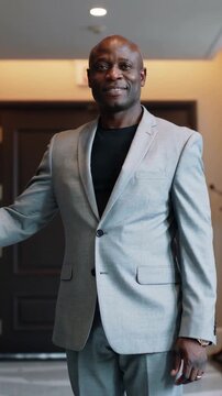 Vertical video: Holding brass handle, man in light-gray suit stepping into foyer, welcoming guests