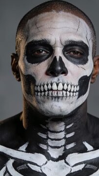 Vertical video: Camera starting, man with skull paint opening eyes in studio, bare-chested